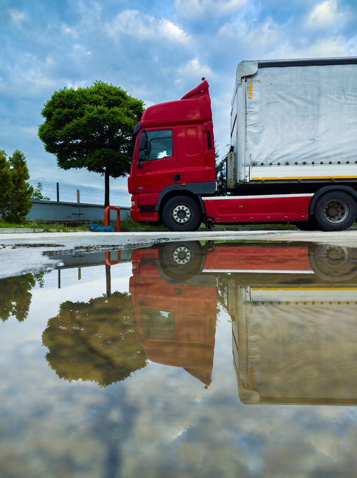Mastering the First Impression: Your intriguing post title goes here A parked red truck with a tarp-covered cargo is reflected in a puddle on an urban street, under a cloudy sky.