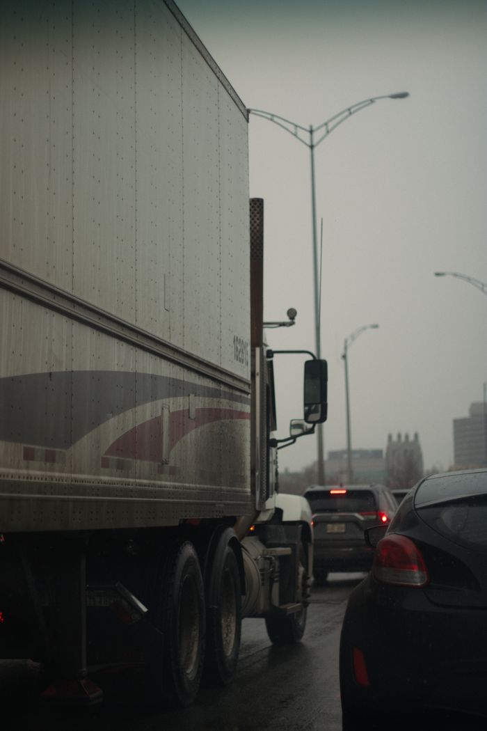 about-us-01 A line of vehicles stuck in traffic on a cloudy urban road.